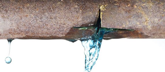 Ein verrostetes Metallrohr, aus dem eine blaue Flüssigkeit tropft.