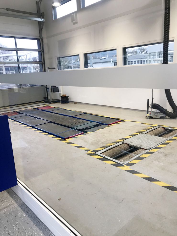 Ein Innenraum, vermutlich eine Werkstatt, einem Schlauch auf der rechten Seite und Fenstern, durch die Tageslicht einfällt.