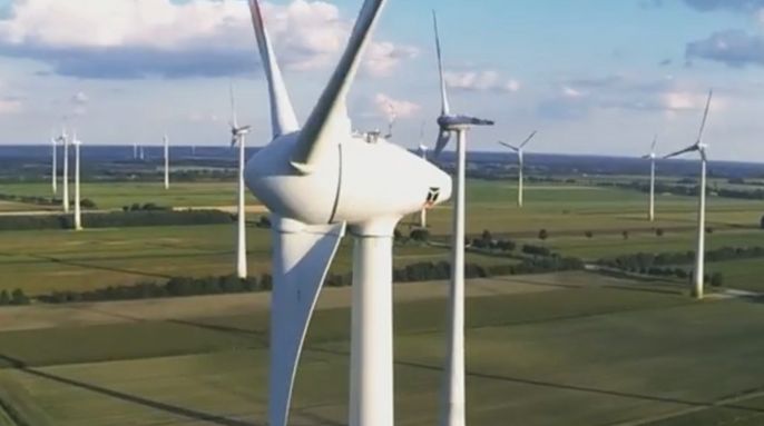 Eine weite Landschaft mit zahlreichen Windturbinen, die sich vor dem Hintergrund des blauen Himmels und der grünen Felder erheben.