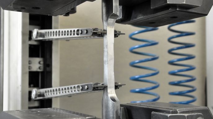 Eine mechanische Vorrichtung mit Metallklammern, einer zentralen Stange und blauen Spiralfedern.
