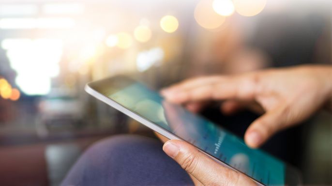 Die Hand einer Person, die ein Tablet hält, auf dessen Bildschirm ein Inhalt angezeigt wird.