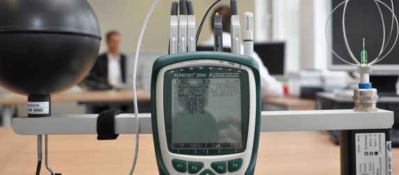 Ein Handheld-Gerät, an das verschiedene Kabel angeschlossen sind und das auf einem Tisch in einem Büro steht.