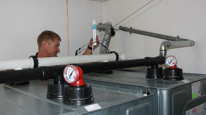 Ein Mann arbeitet an einem Heizöltank mit verschiedenen Rohren, Ventilen und einem Druckmesser.