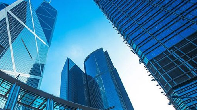 Moderne Wolkenkratzer mit spiegelnden Glasfassaden, die durch einen transparenten Gehweg miteinander verbunden sind, vor einem strahlend blauen Himmel.